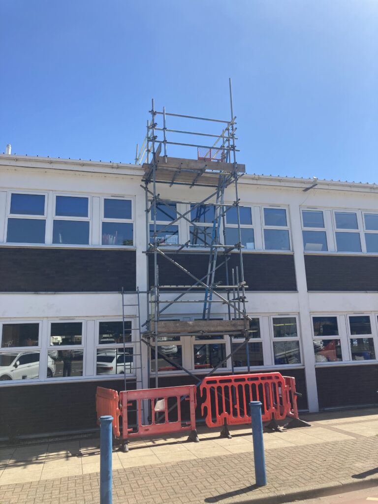 scaffolding with ladder on side of building for roof access - red barriers at bottom